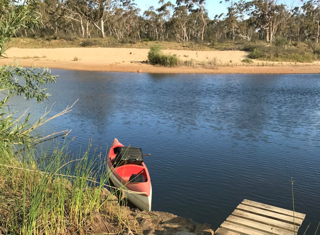 Red canoe on river with large trolley bag by Ray Monde