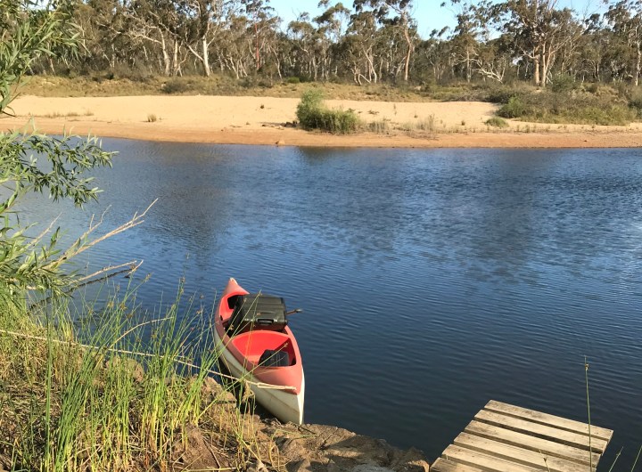 Red canoe on river with large trolley bag by Ray Monde