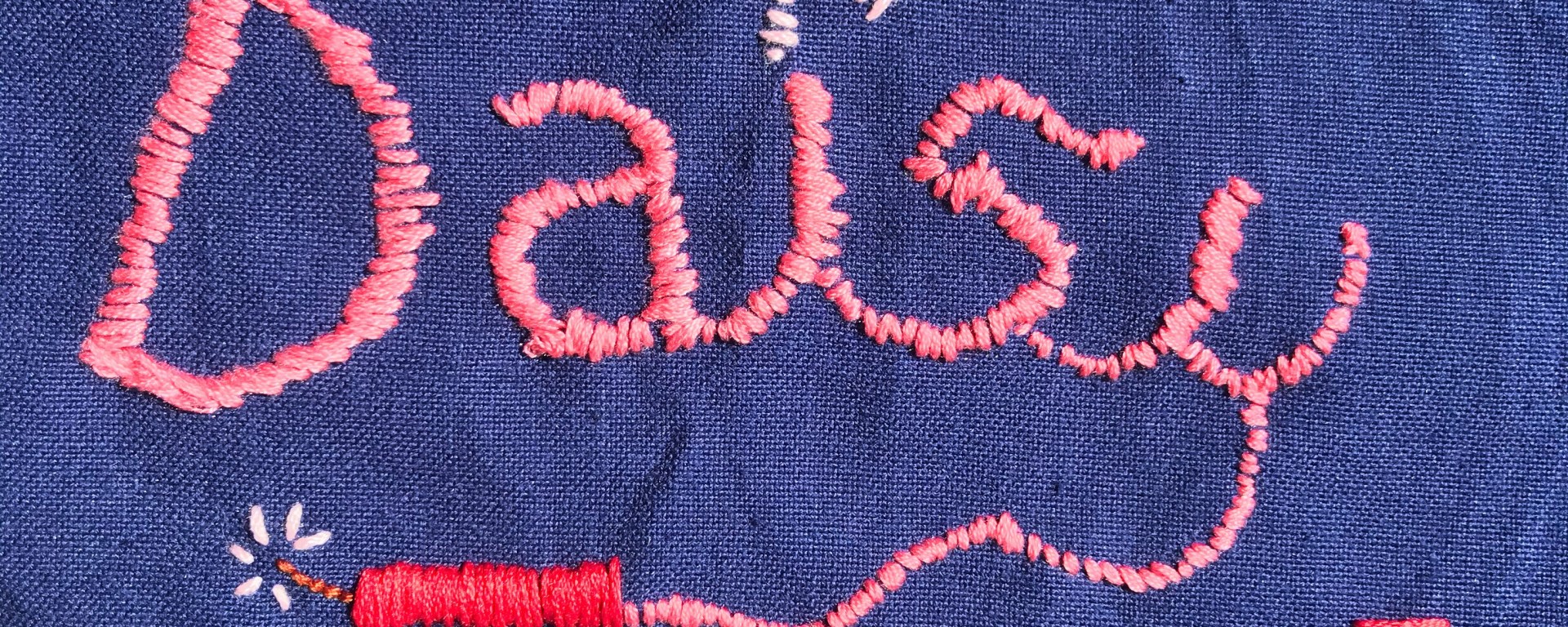 Pink embroidery on blue fabric with the name DAISY