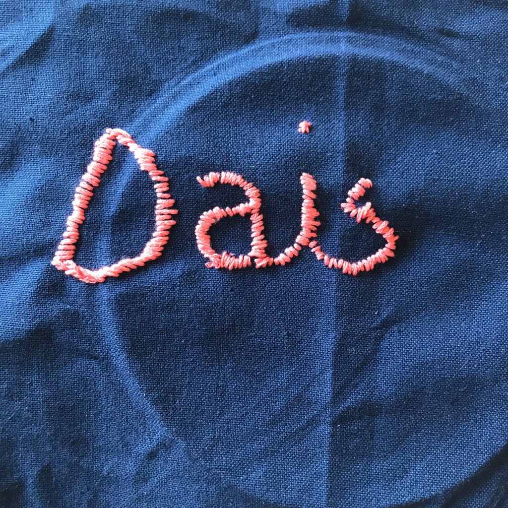 A blue piece of cloth with pink stitching which reads Dais