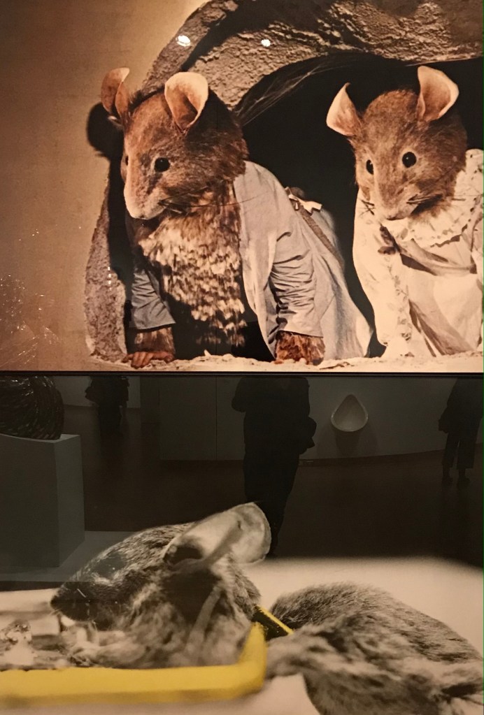Artwork by John Baldessari showing two puppet mice overlooking a real dead mouse in a trap