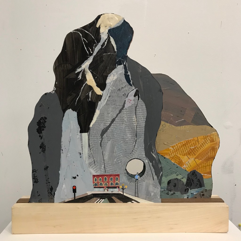 A paper sculpture by Ray Monde of tall mountains with a hole cut through them